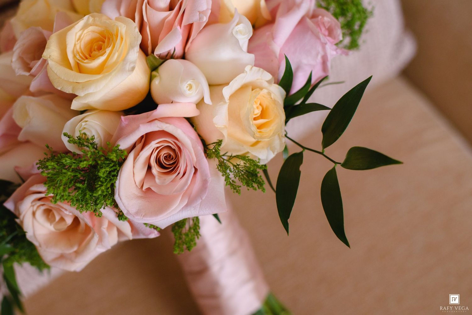 Elegant bridal bouquet of soft pink and peach roses with green foliage, wrapped in pink ribbon.