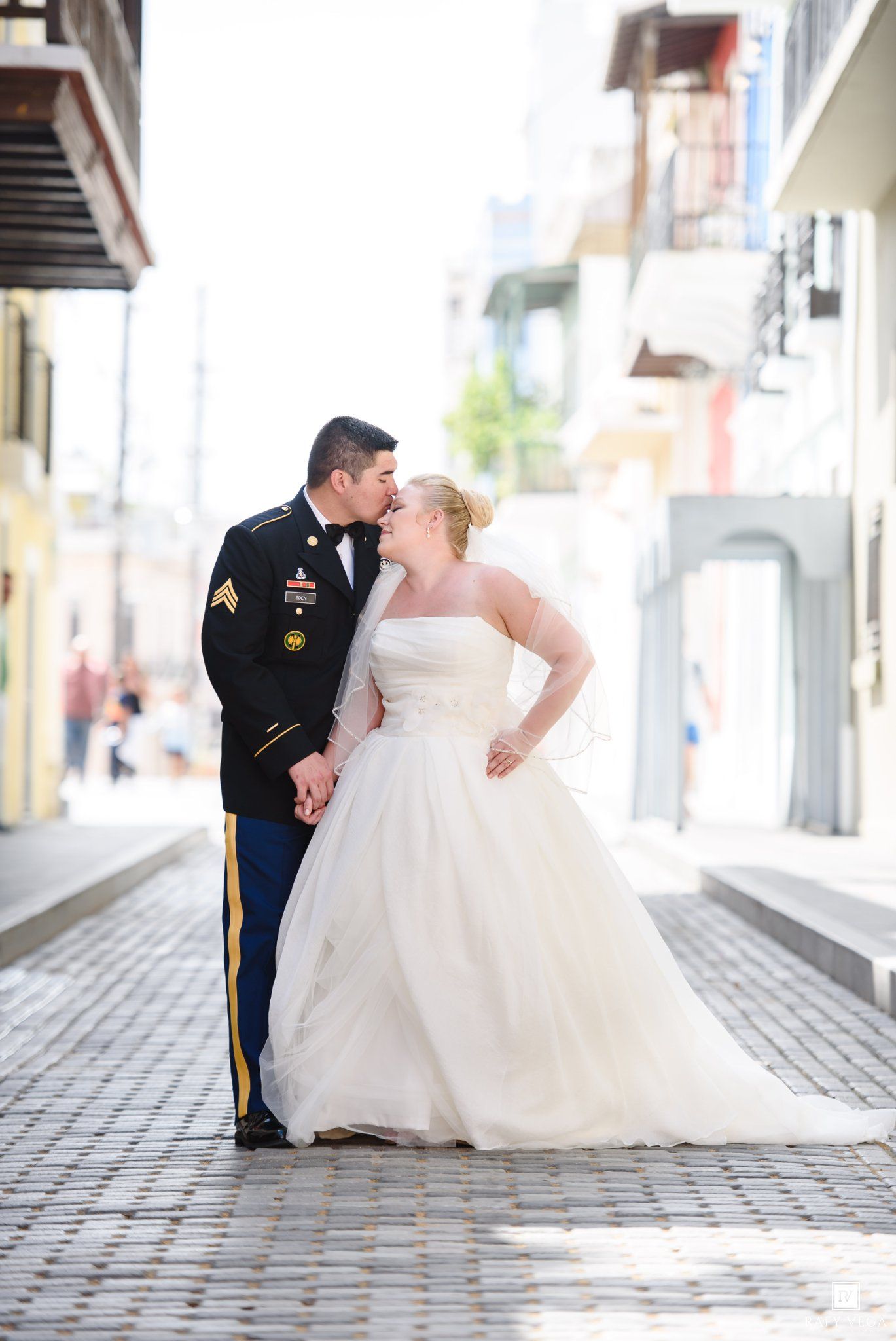 Military groom in dress uniform kisses bride in white ball gown on cobblestone street in Old San Juan.