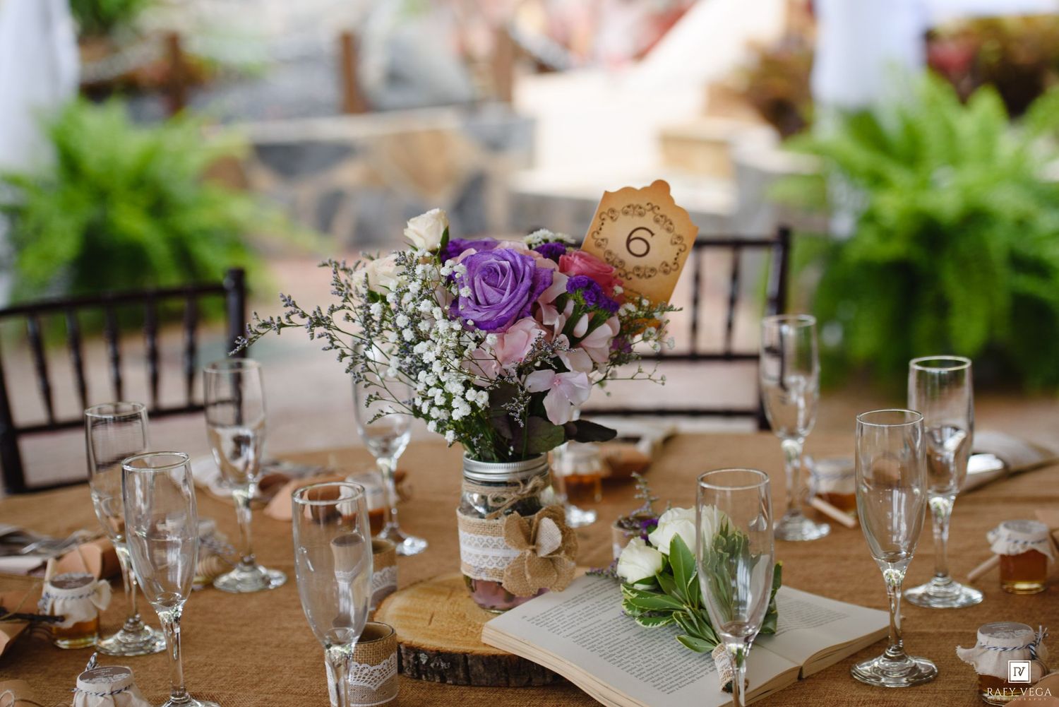 Rustic wedding reception table with purple and white floral centerpiece, glassware, and burlap accents.