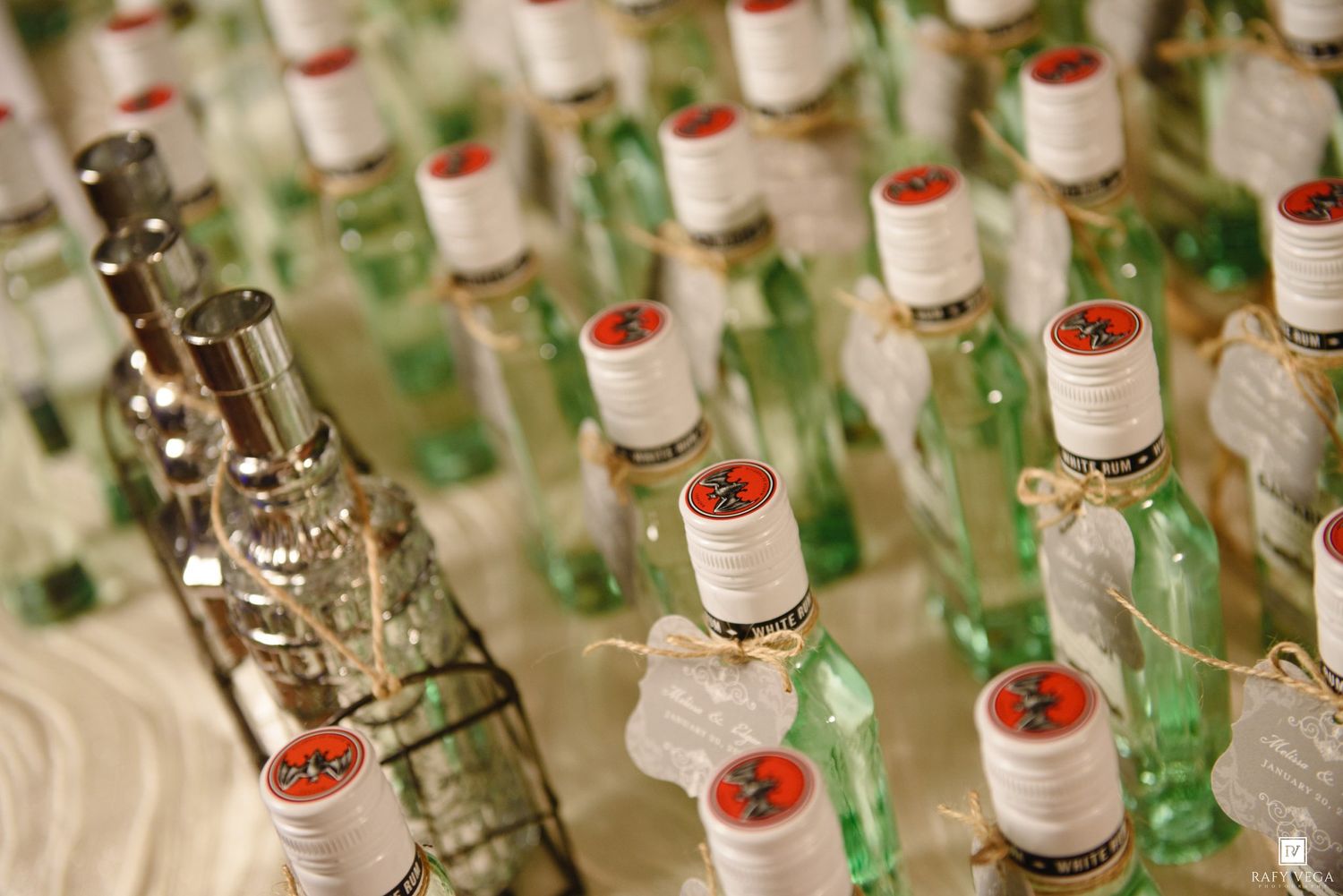 Rows of green glass liquor bottles with red caps and white labels displayed on a table at an event.
