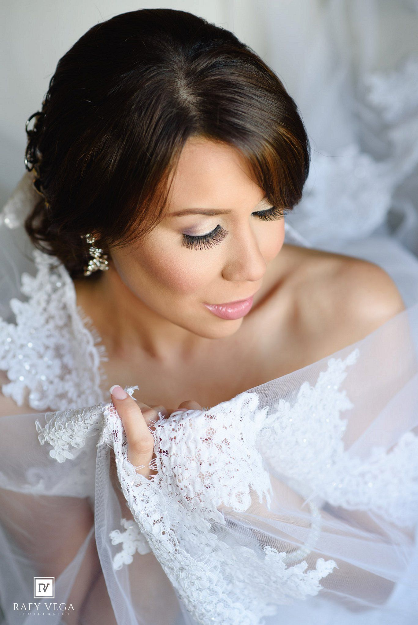 Beautiful bride in lace off-shoulder wedding gown with updo hairstyle and glamorous bridal makeup.