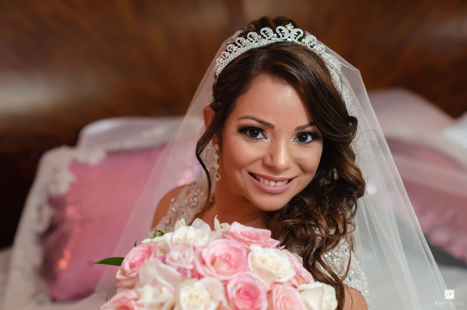 Smiling bride wearing tiara and veil holds pink and white rose bouquet on her wedding day.
