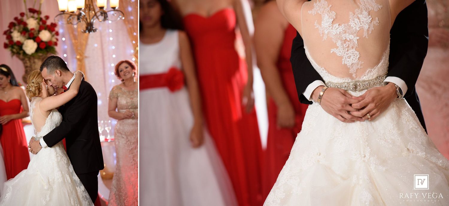 Bride and groom share first dance at wedding reception with bridesmaids in red dresses in background.