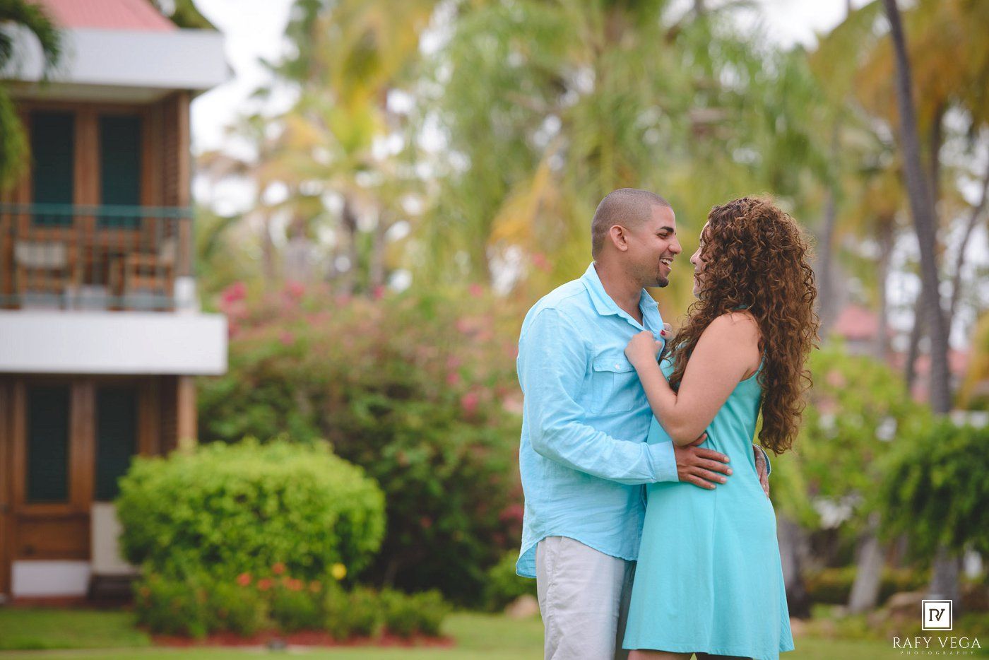 Couple in matching turquoise outfits sharing a romantic moment in a tropical garden resort setting.