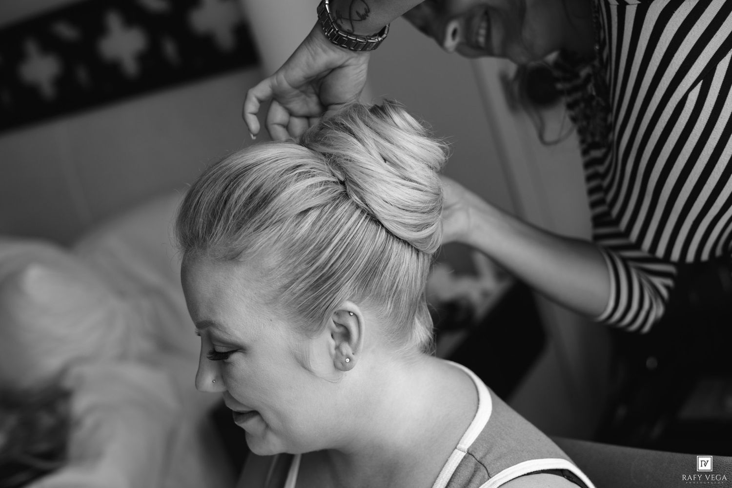 Black and white photo of a hairstylist styling a blonde woman's hair into an updo for a wedding.