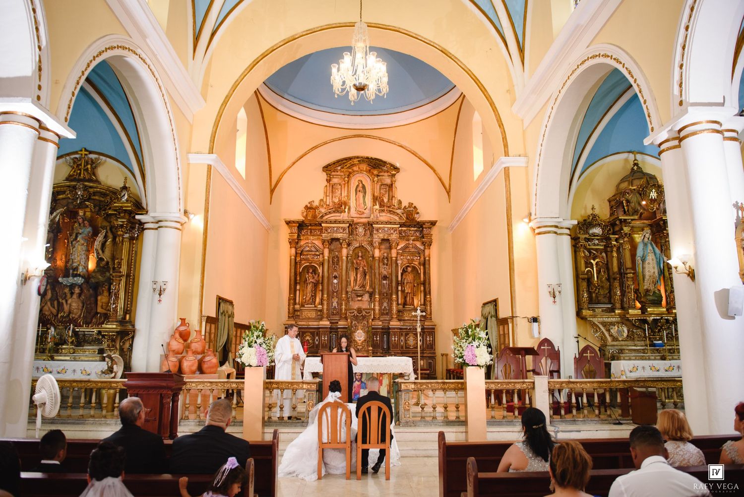 Beautiful Catholic church wedding ceremony at ornate golden altar with bride and groom.