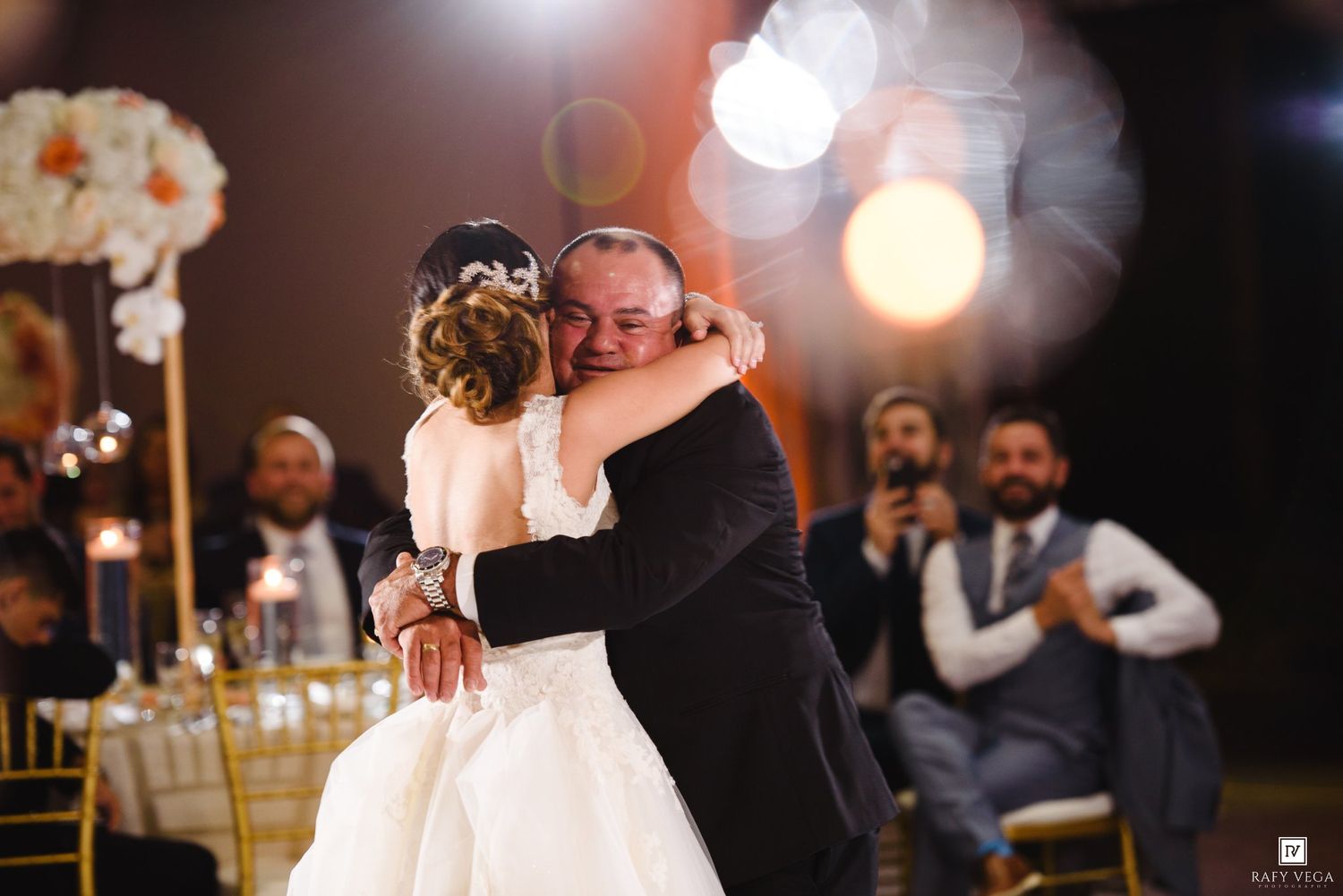 Bride and father share emotional first dance hug at elegant wedding reception with golden chairs and floral arrangements.