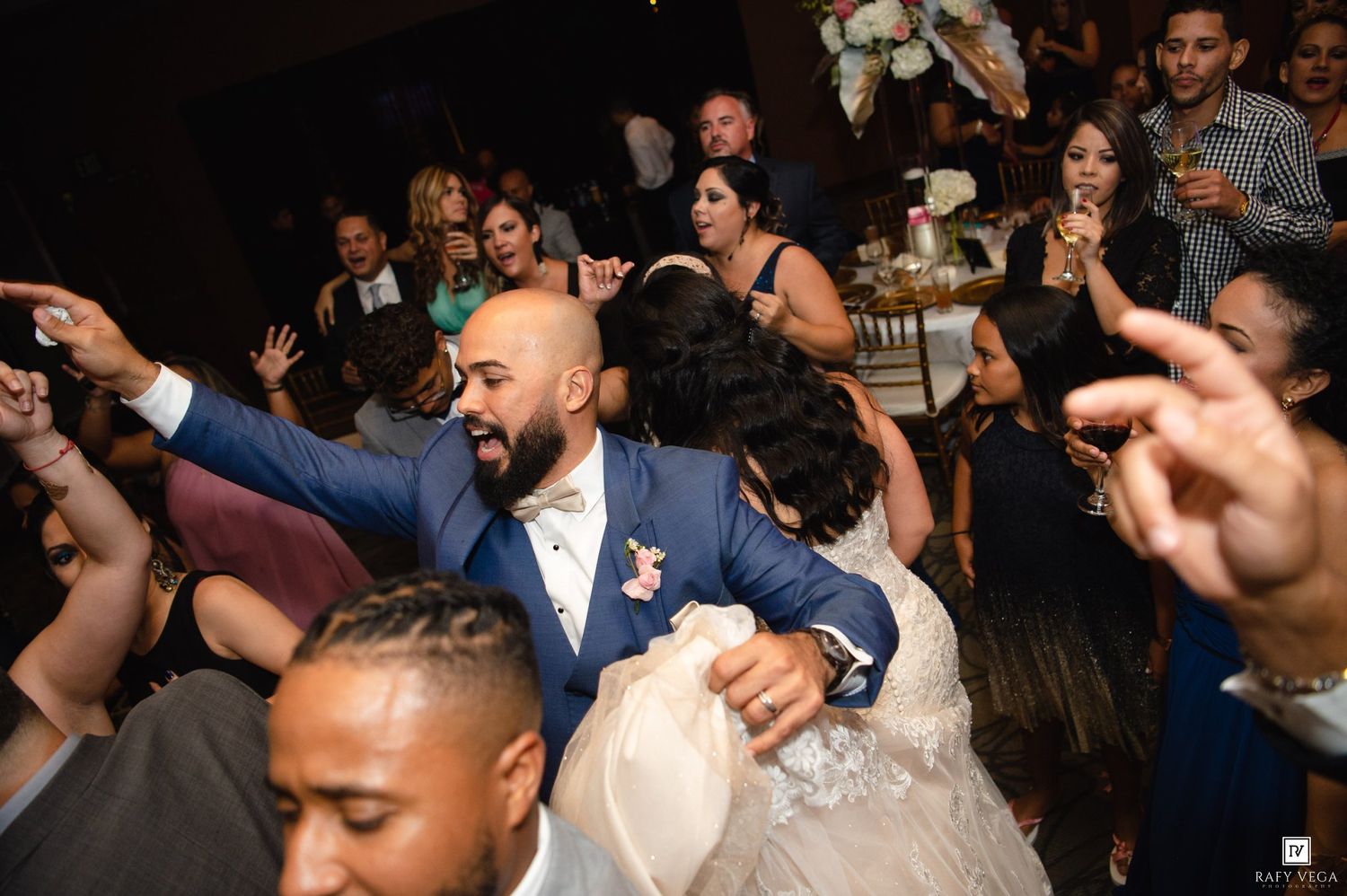 Bride and groom dancing joyfully with wedding guests on a crowded reception dance floor.
