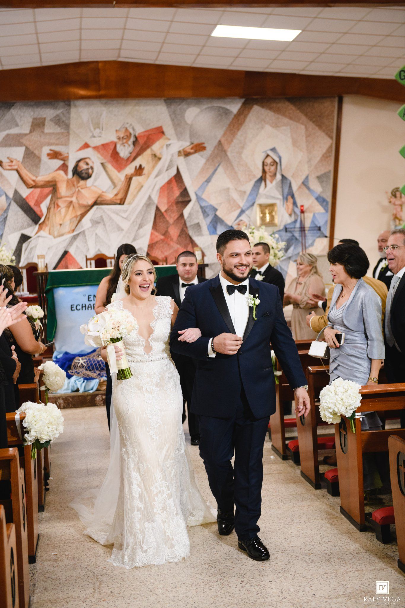 Bride and groom walking down the aisle after wedding ceremony in a church with colorful mural.