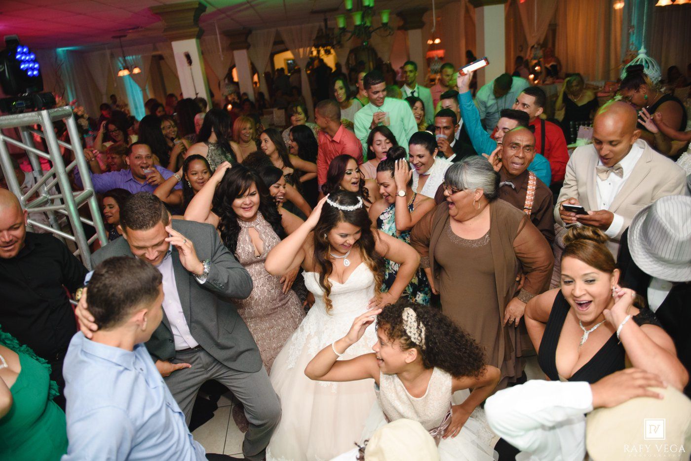 Joyful quinceañera celebration with guests dancing and cheering around the birthday girl in a white ballgown.