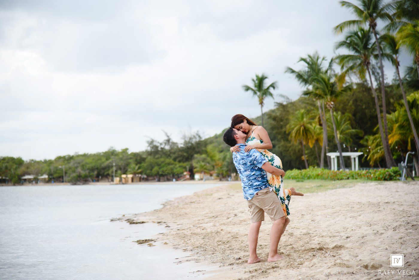 Couple embracing on a tropical beach with palm trees and calm waters in the background.