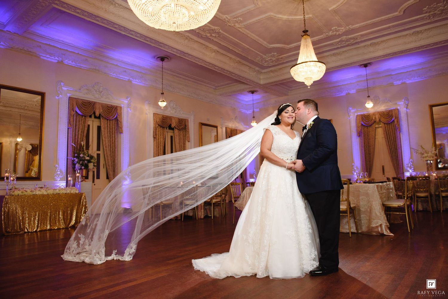 Bride and groom share romantic first dance as her cathedral veil flows dramatically in ornate ballroom.