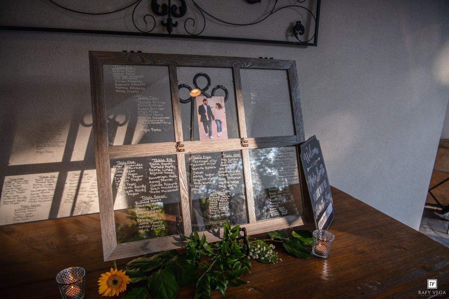 Wedding memory display with photos and handwritten notes on glass panes, adorned with fresh flowers on a wooden table.