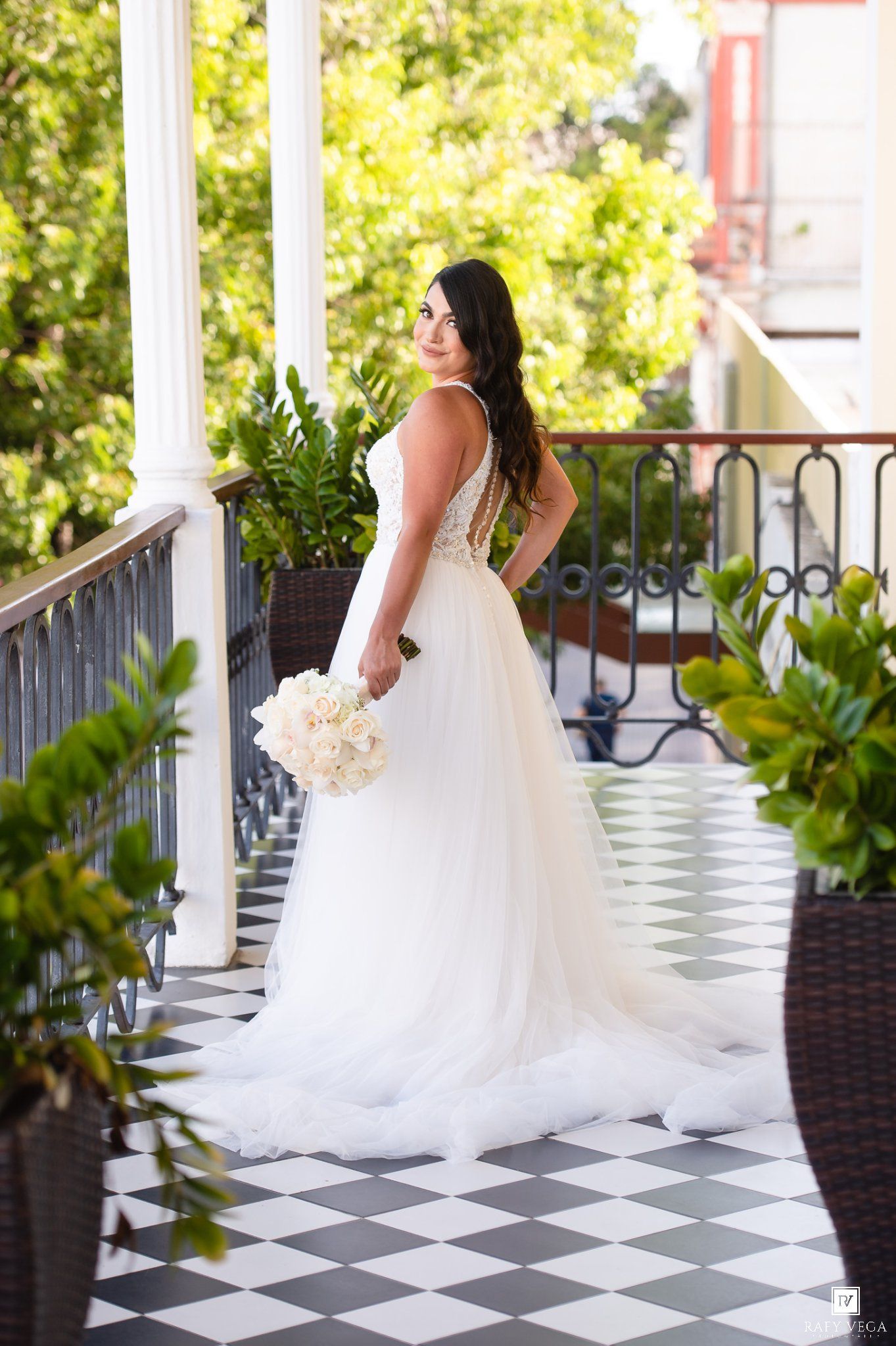 Bride in white tulle wedding gown holding bouquet on elegant black and white checkered balcony.