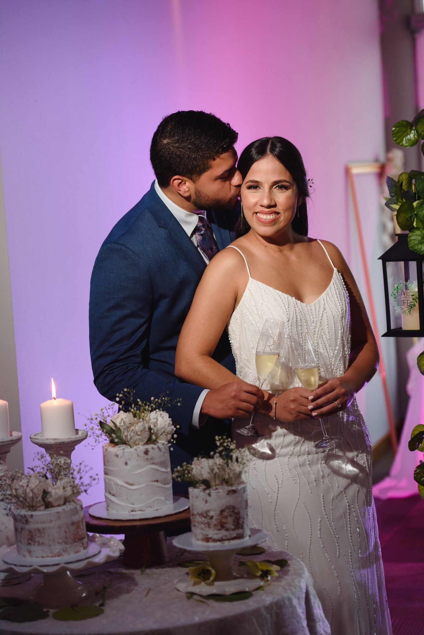 Bride and groom toasting with champagne glasses beside a white wedding cake at their elegant reception.