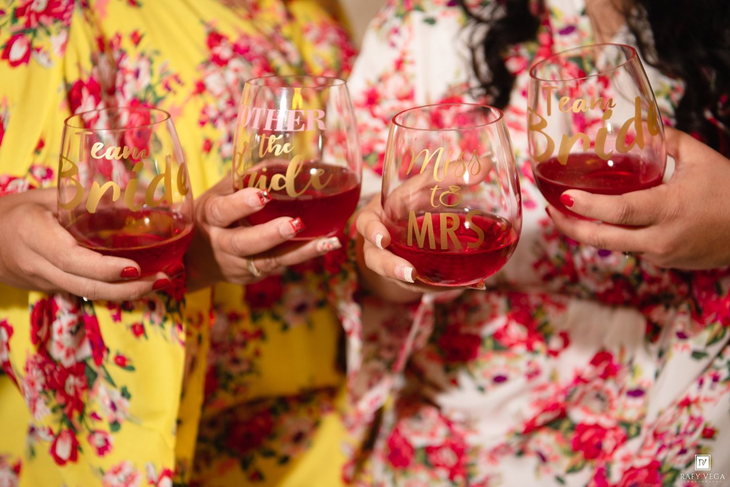 Bridesmaids in floral robes toasting with stemless wine glasses labeled Miss to Mrs at a bridal party celebration.