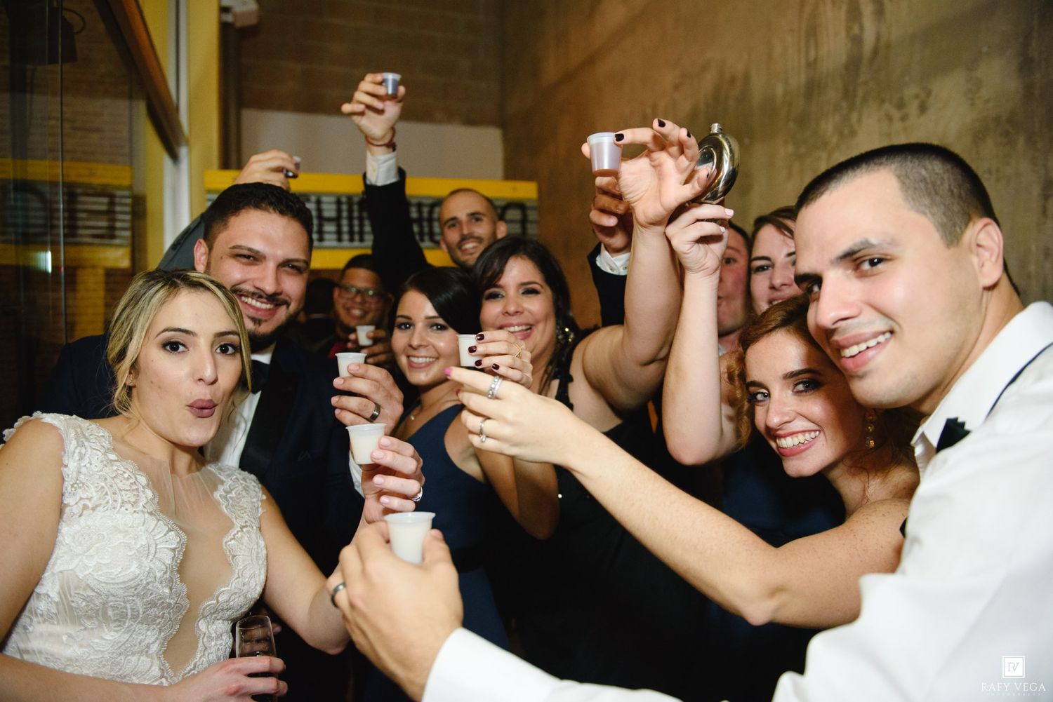 Wedding party toasting with drinks and phones raised in celebration at reception.