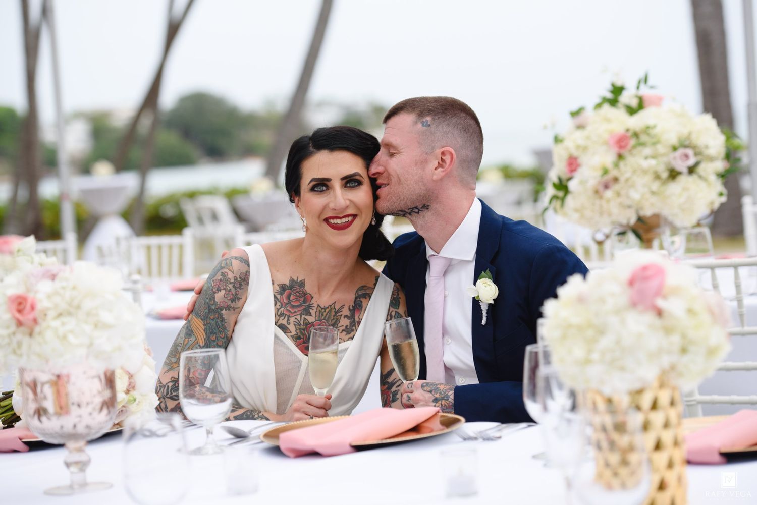 Bride and groom share a romantic moment at their elegant outdoor wedding reception with pink floral centerpieces.
