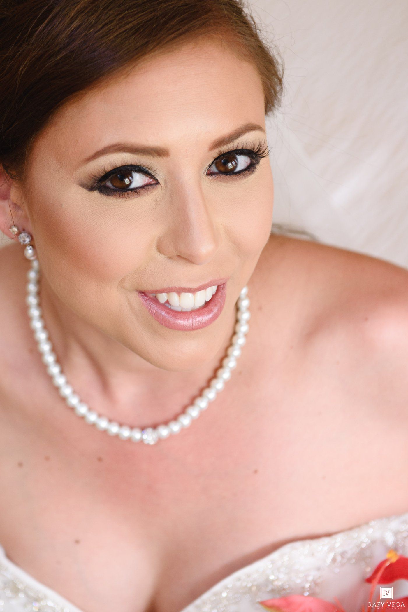 Beautiful bride smiling in a white lace gown with pearl necklace and earrings and elegant makeup.