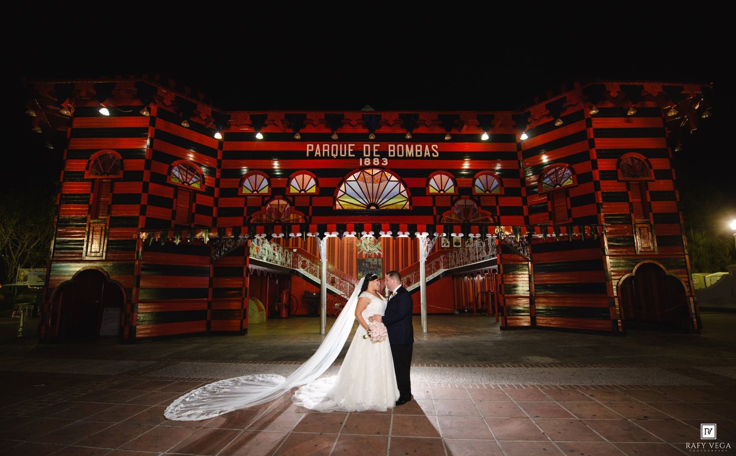Bride and groom kissing at night in front of the iconic red and black Parque de Bombas building in Ponce, Puerto Rico.