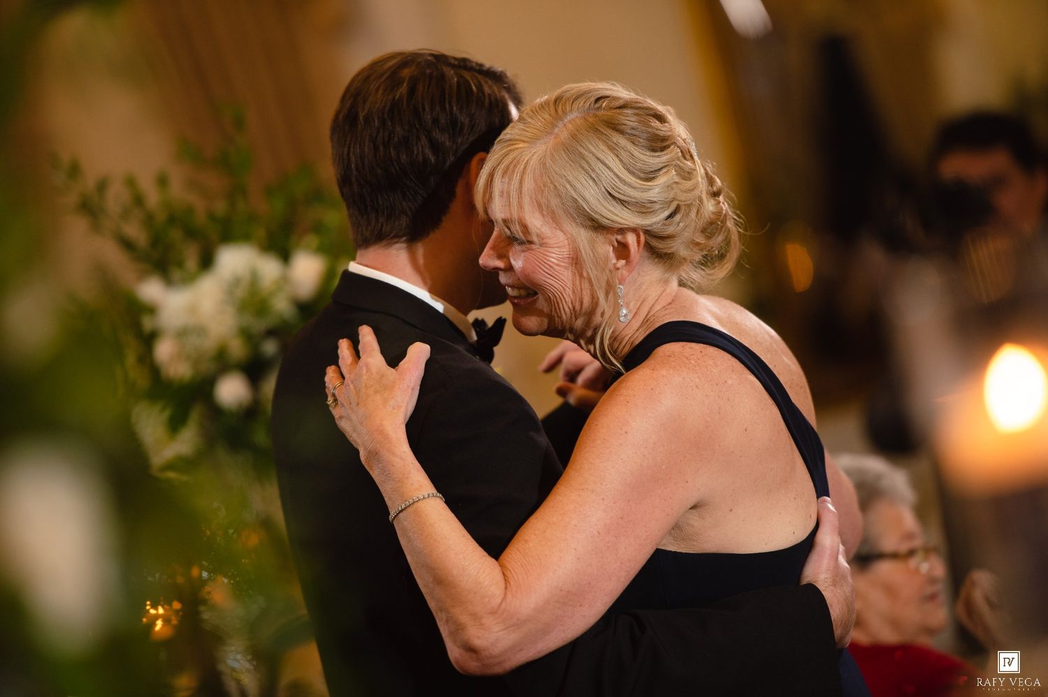 Emotional mother and son share a tender dance embrace at an elegant wedding reception.