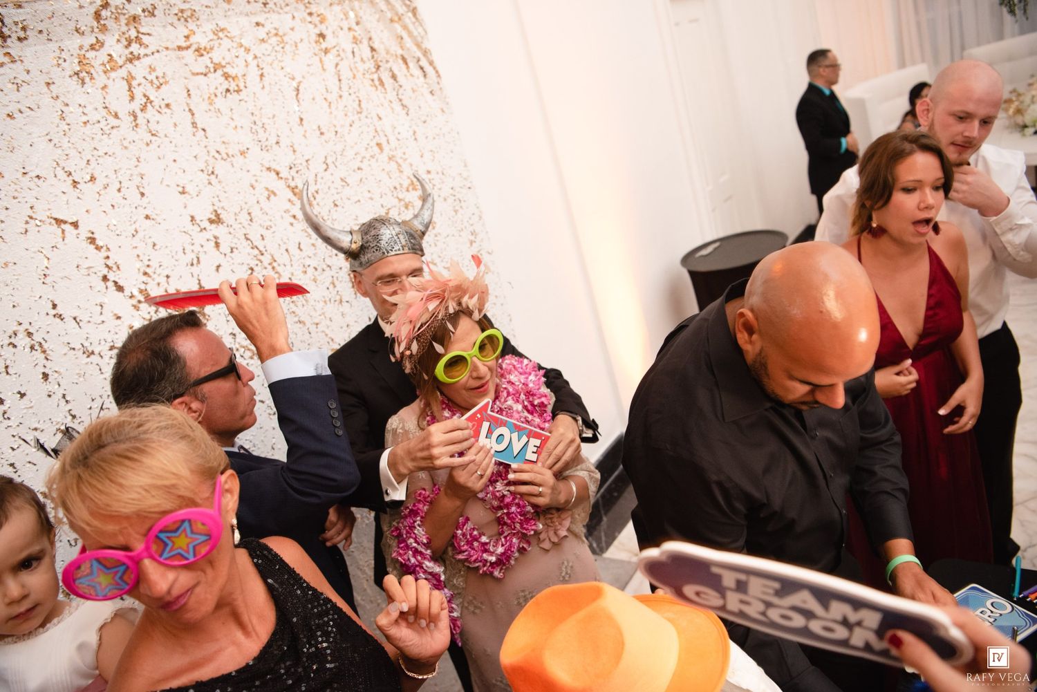 Guests wearing fun props and costumes at a lively wedding reception photo booth celebration.