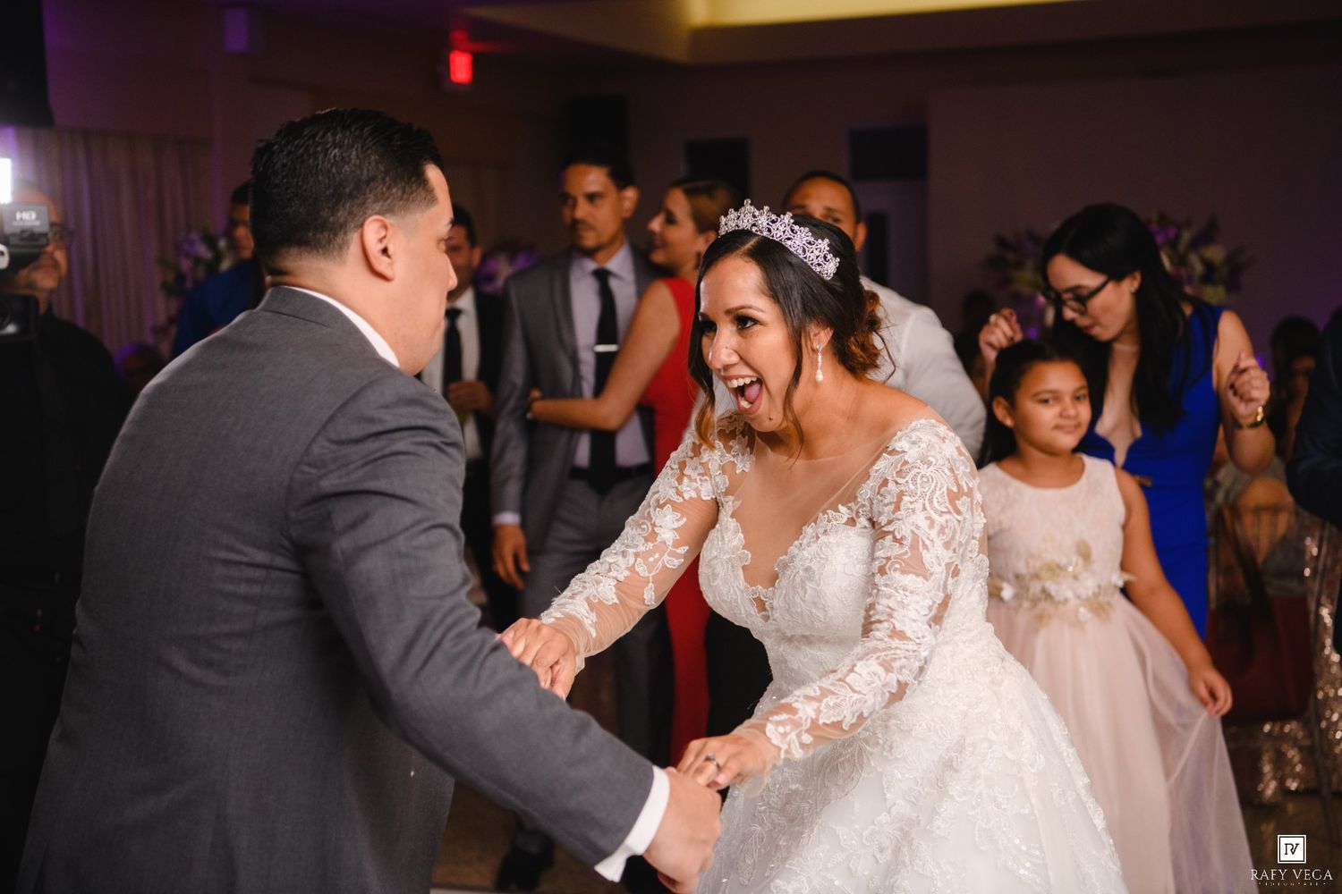 Bride in lace ball gown dancing joyfully with groom at elegant wedding reception.