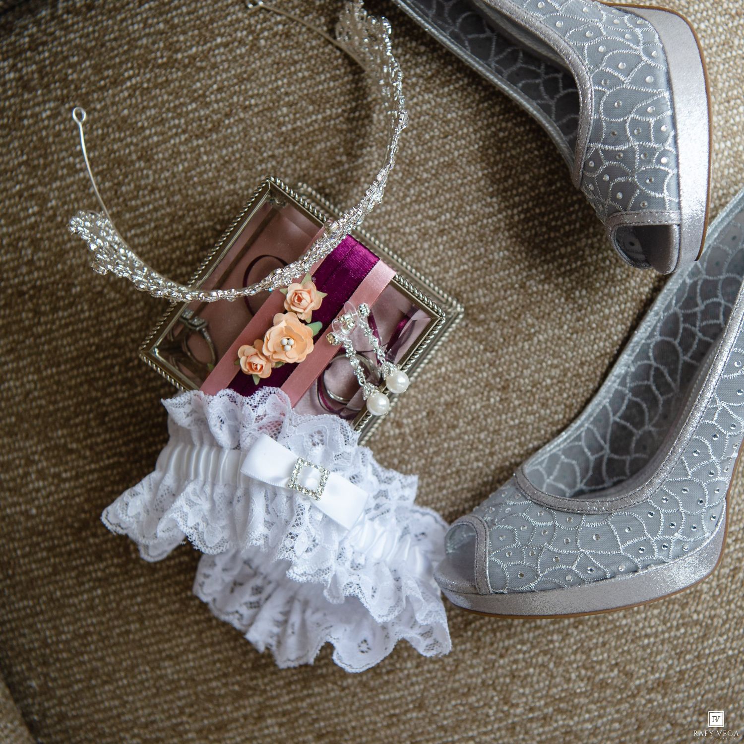 Gray crackle-pattern heels, white lace bridal garter, rhinestone tiara, and elegant jewelry displayed on carpet.