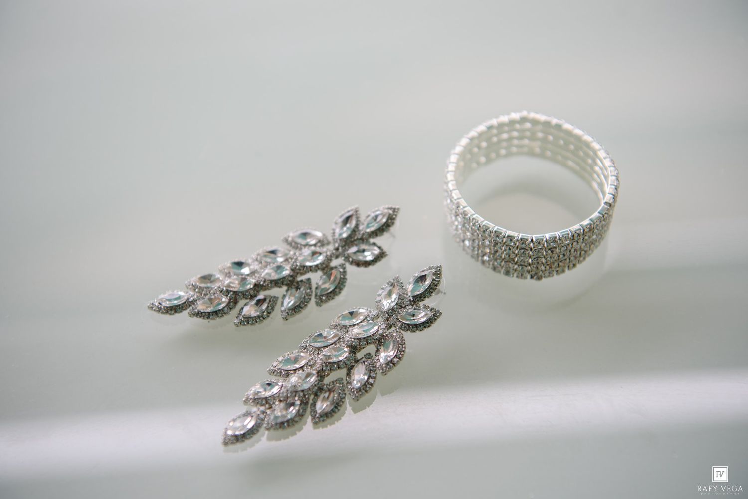 Elegant crystal drop earrings and pearl rhinestone bracelet on white surface, perfect bridal jewelry set.