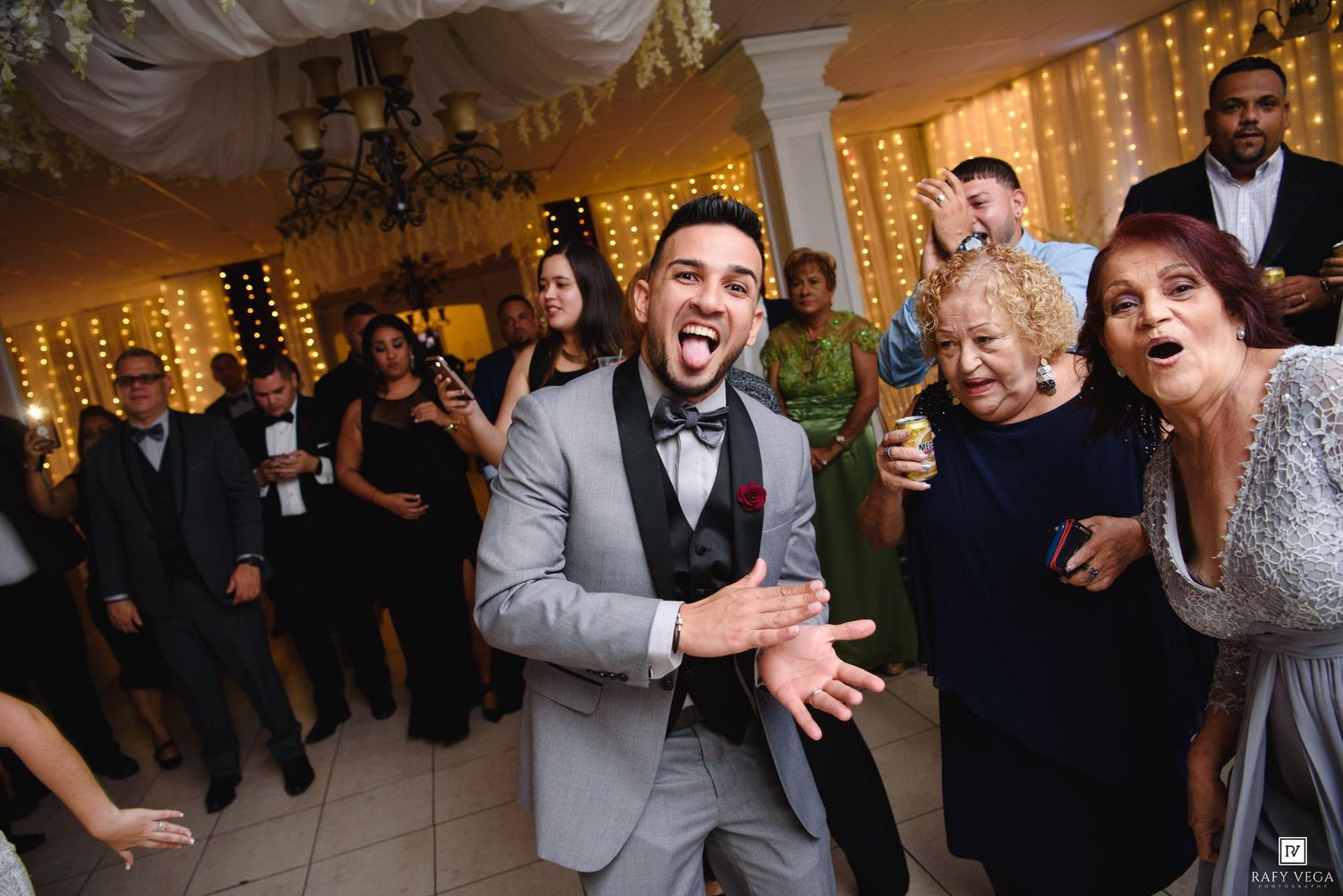 Groom in gray suit laughing with elderly female guests on decorated wedding reception dance floor.