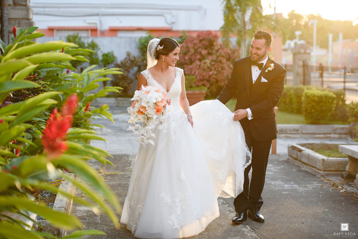 Bride in white ball gown and groom in tuxedo share a romantic moment in a lush garden on their wedding day.