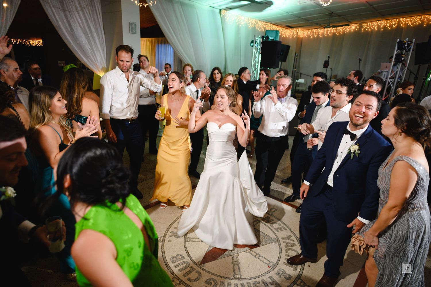 Bride and groom dancing joyfully with guests at a lively wedding reception on a decorated dance floor.