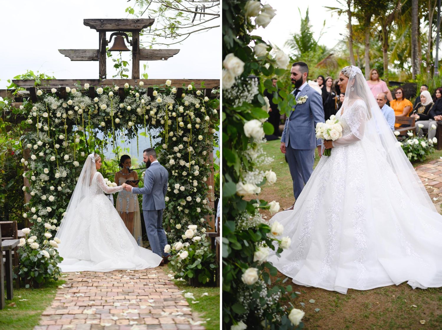 Bride in lace gown exchanges vows with groom in gray suit under floral arch with white roses outdoors.