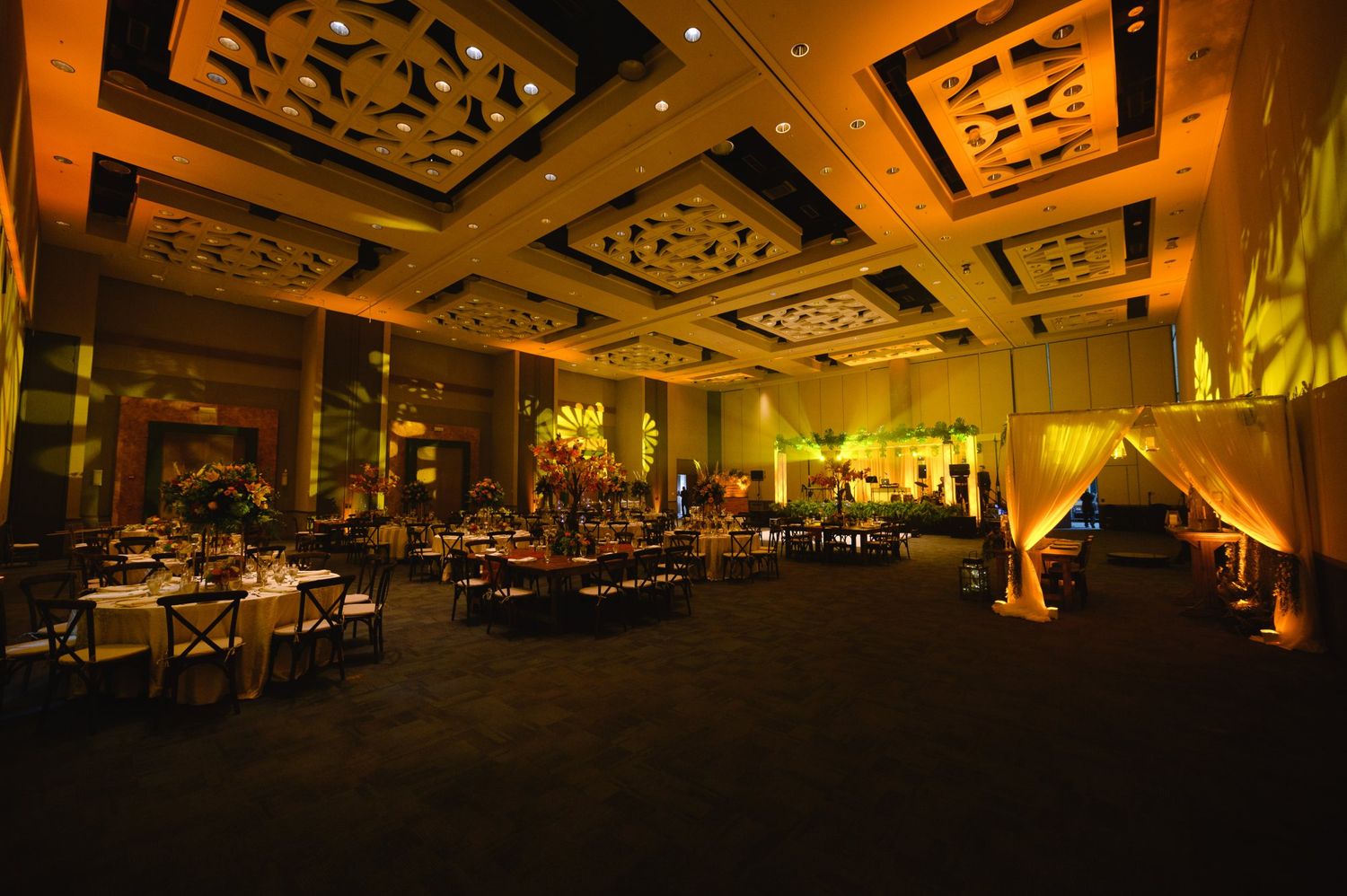 Elegant ballroom event venue with warm golden lighting, ornate ceiling details, and banquet tables set for a formal celebration.