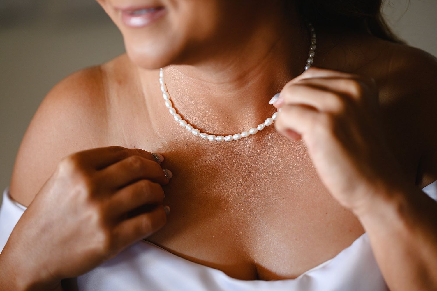 Bride adjusting pearl necklace while wearing white strapless gown, elegant bridal jewelry detail.