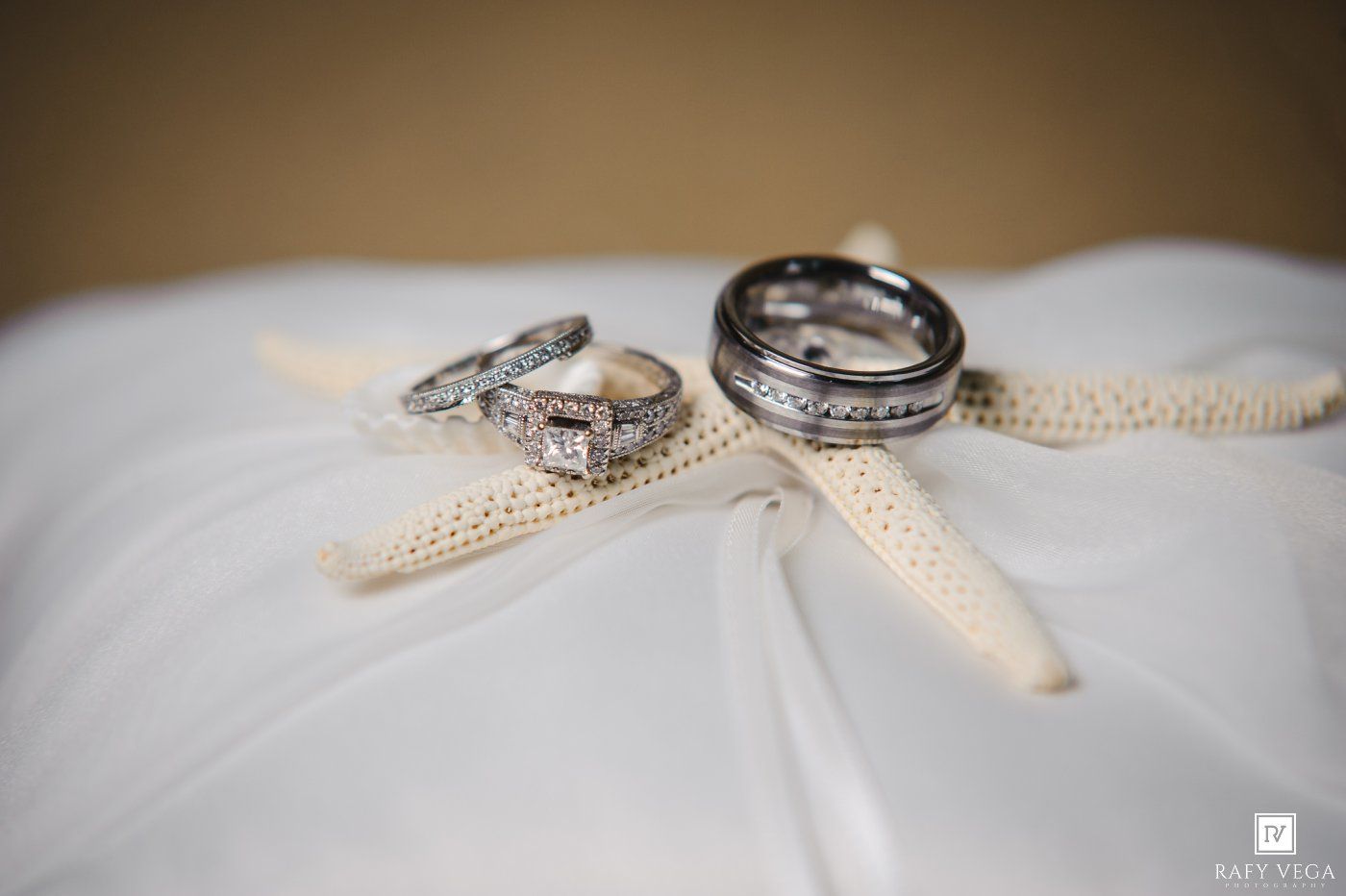 Wedding rings and bands displayed on a white pillow with starfish, perfect for a beach-themed ceremony.