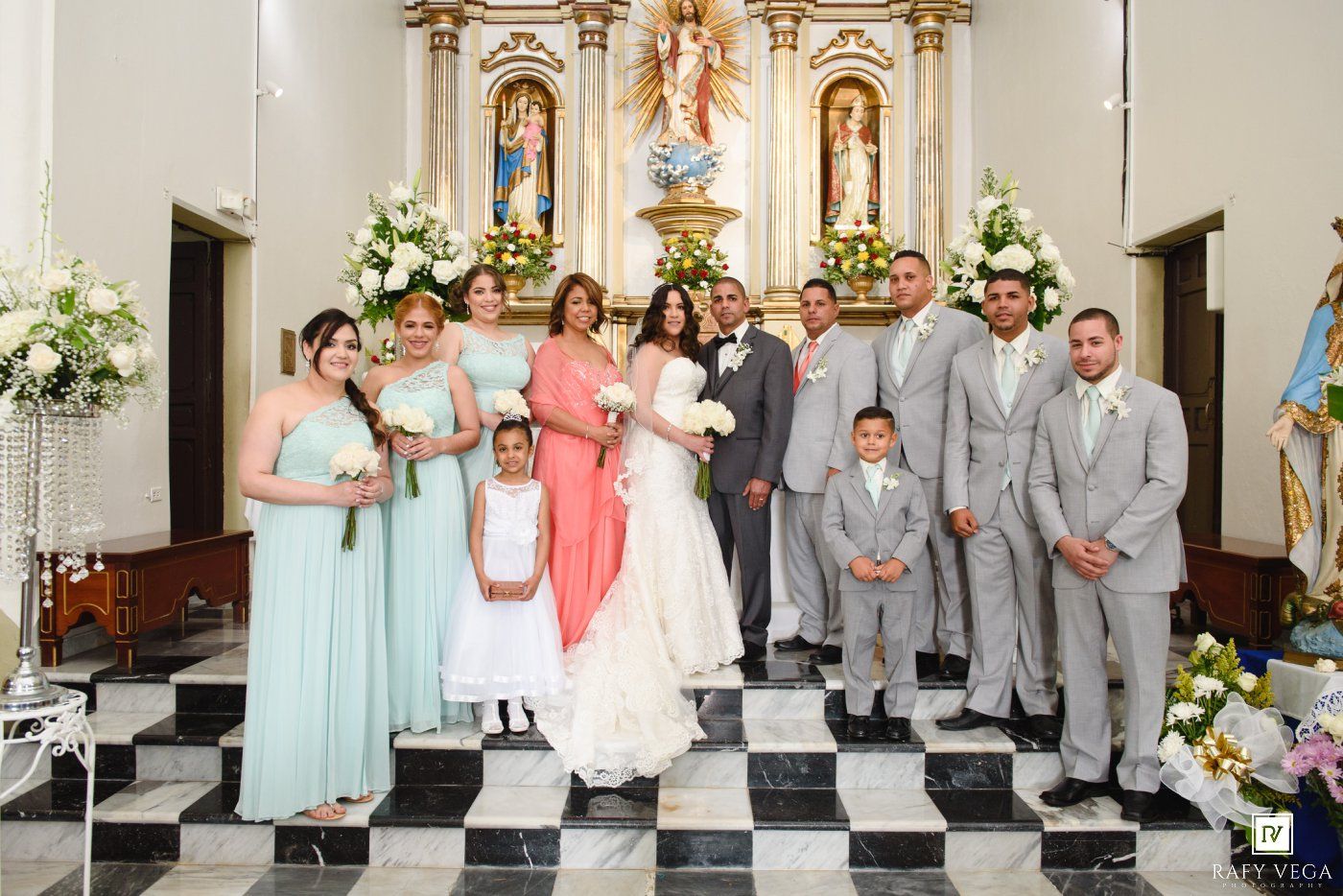 Wedding party poses at church altar with bridesmaids in mint gowns and groomsmen in gray suits.