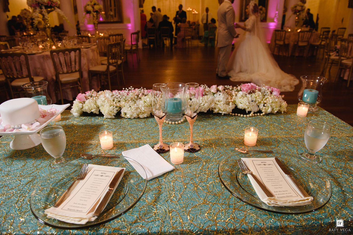Elegant wedding reception table with teal sequin tablecloth, floral centerpiece, candles, and menus at a ballroom venue.