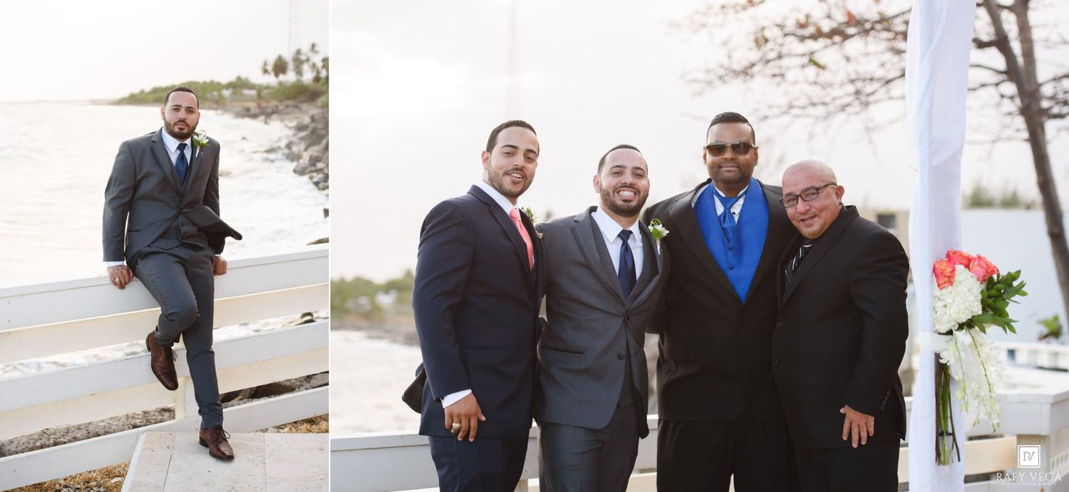 Groomsmen in navy suits pose outdoors near waterfront at a wedding ceremony with floral decorations.