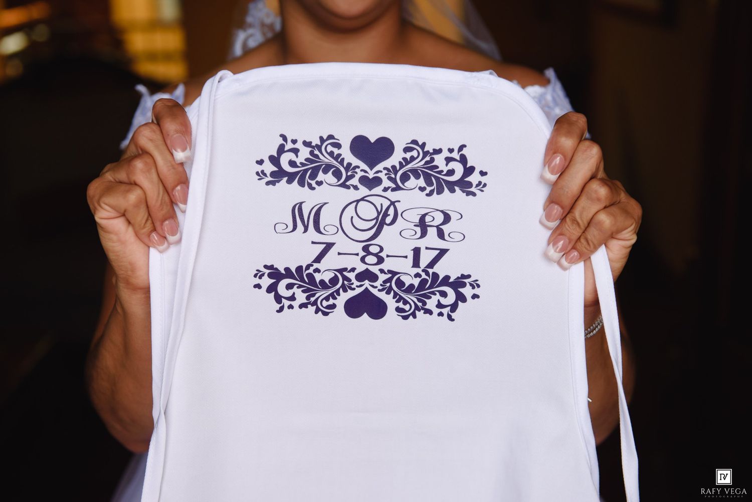 Bride holding white wedding sash with purple monogram MCR 7-8-17 and decorative floral design.