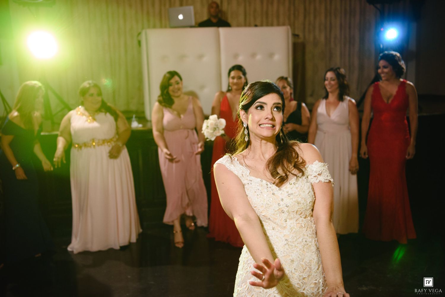 Bride in white lace gown prepares to toss bouquet as bridesmaids in pink dresses eagerly wait behind her.