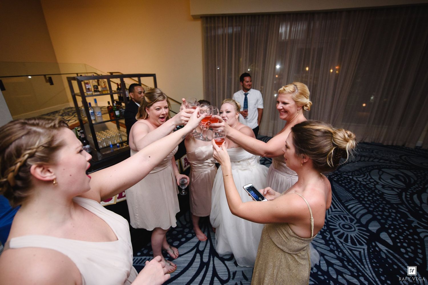 Bridesmaids in white dresses and bride toasting with pink drinks at a wedding reception party.