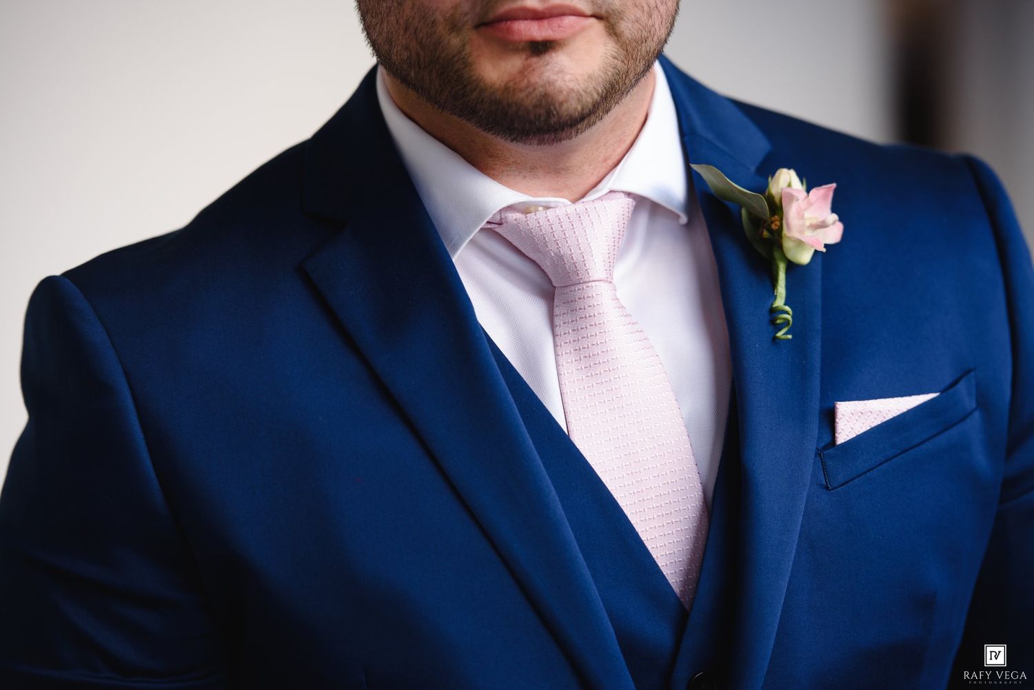 Close-up of groom in navy suit with pink tie, pocket square, and floral boutonniere.