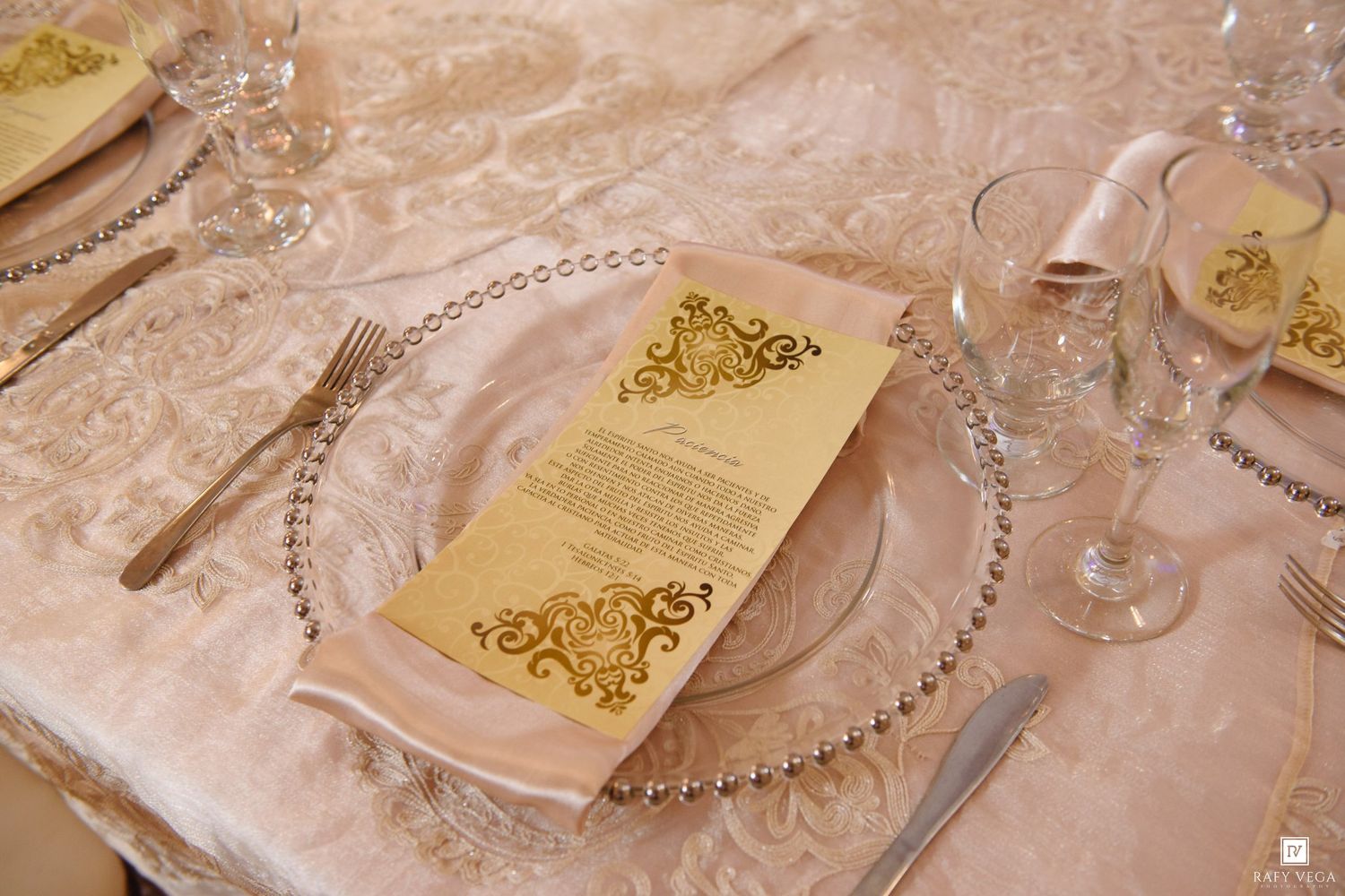 Elegant wedding table setting with gold ornate menu card on beaded charger plate with crystal glassware.