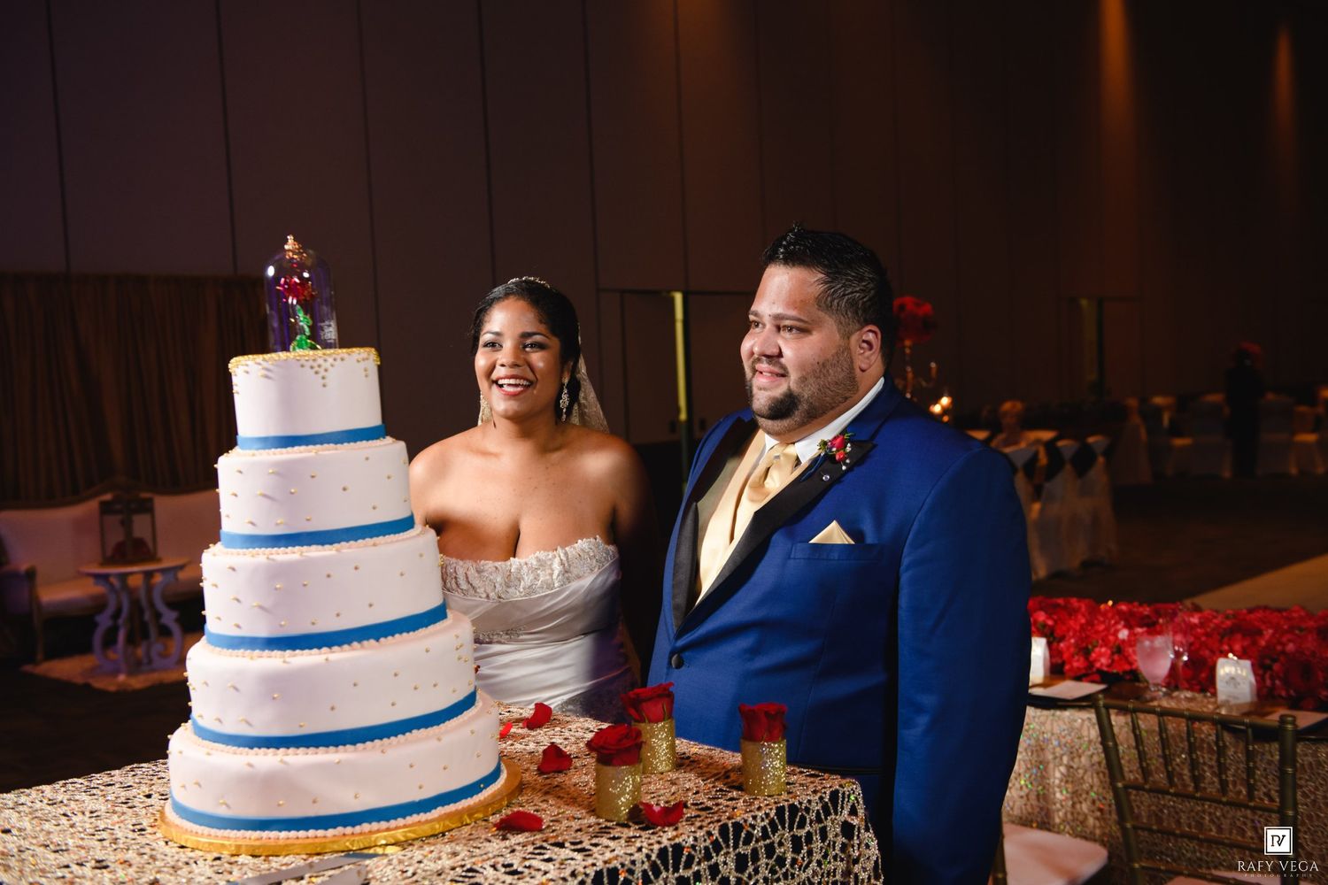 Bride and groom smiling beside a four-tier white wedding cake at their elegant reception venue.