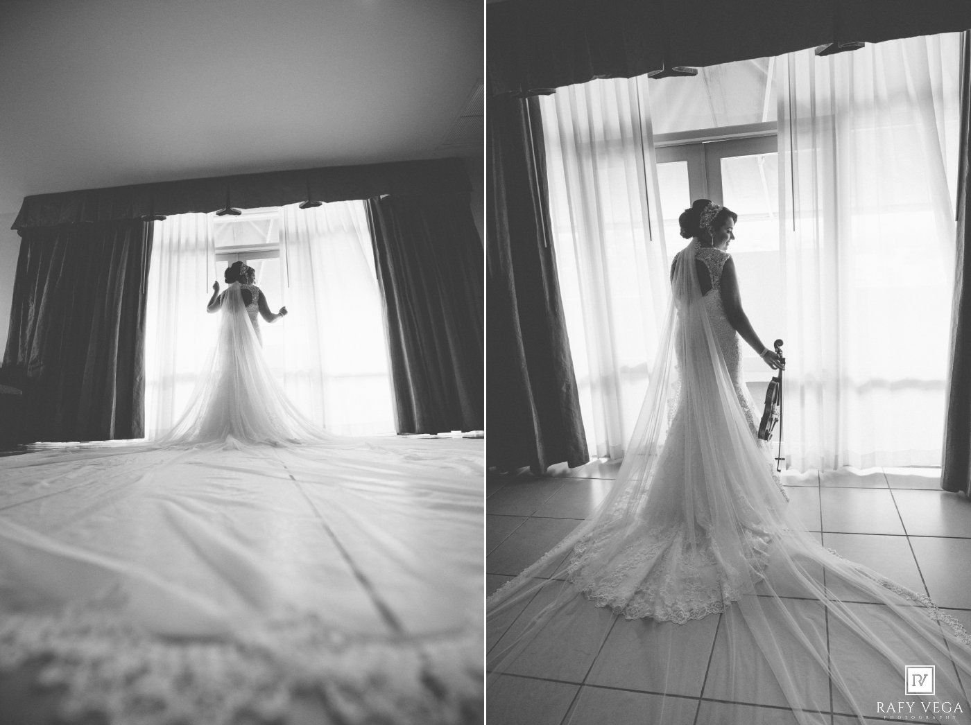 Black and white wedding photo of bride in elegant gown with long veil standing by window in bridal suite.