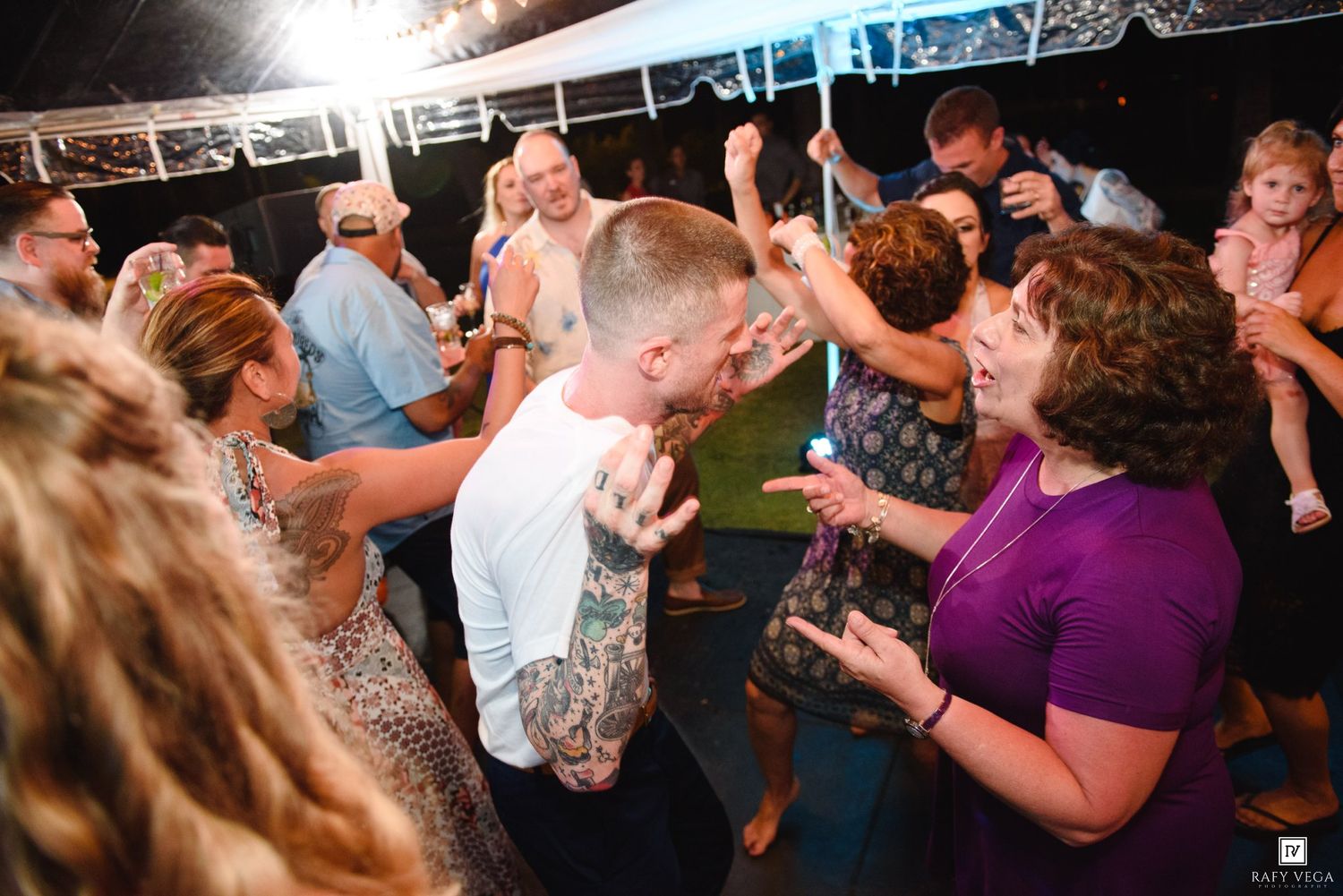 Guests dancing and celebrating at a lively outdoor party event under a tent at night.