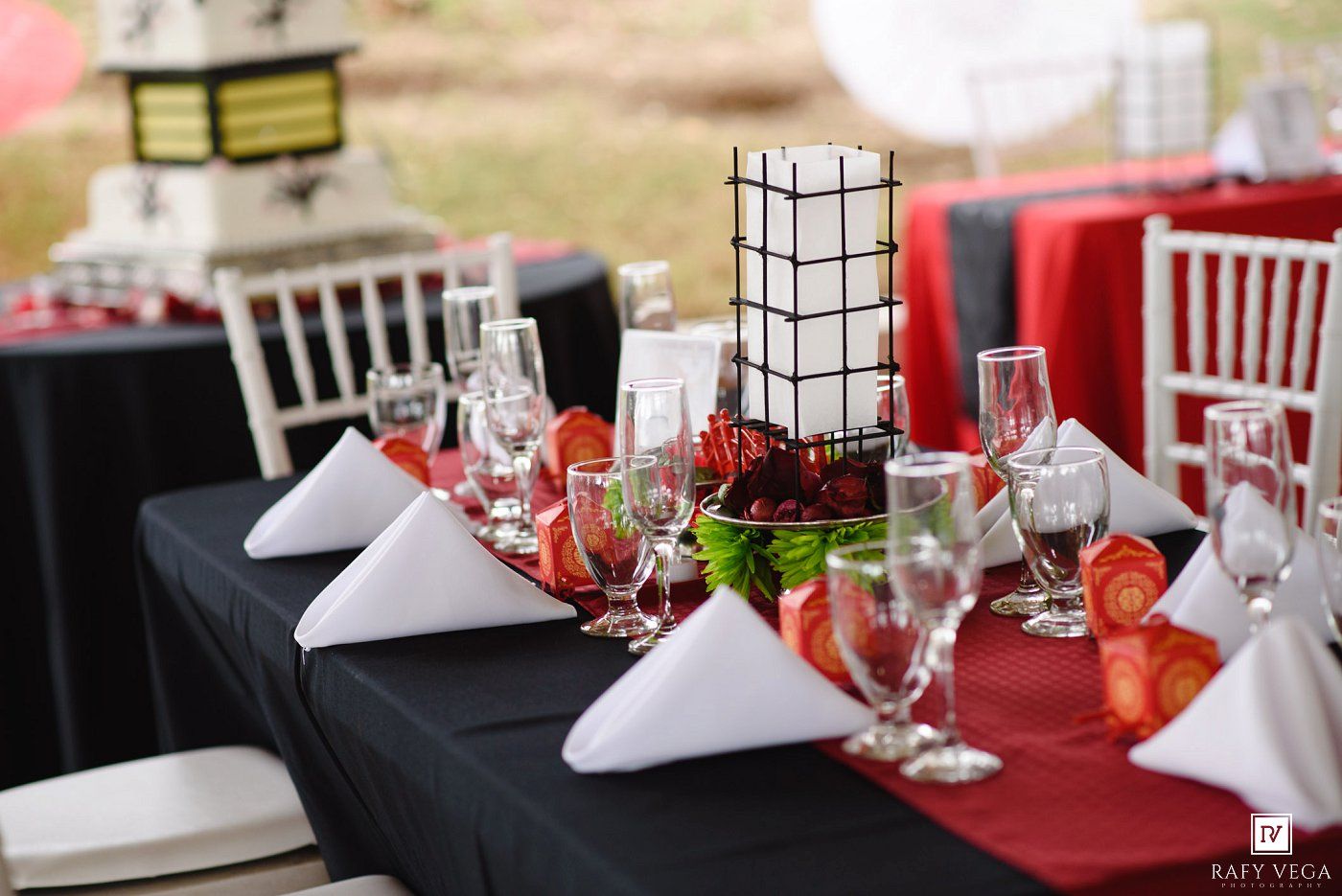 Elegant wedding reception table with black tablecloth, red runner, white napkins, and floral centerpiece.