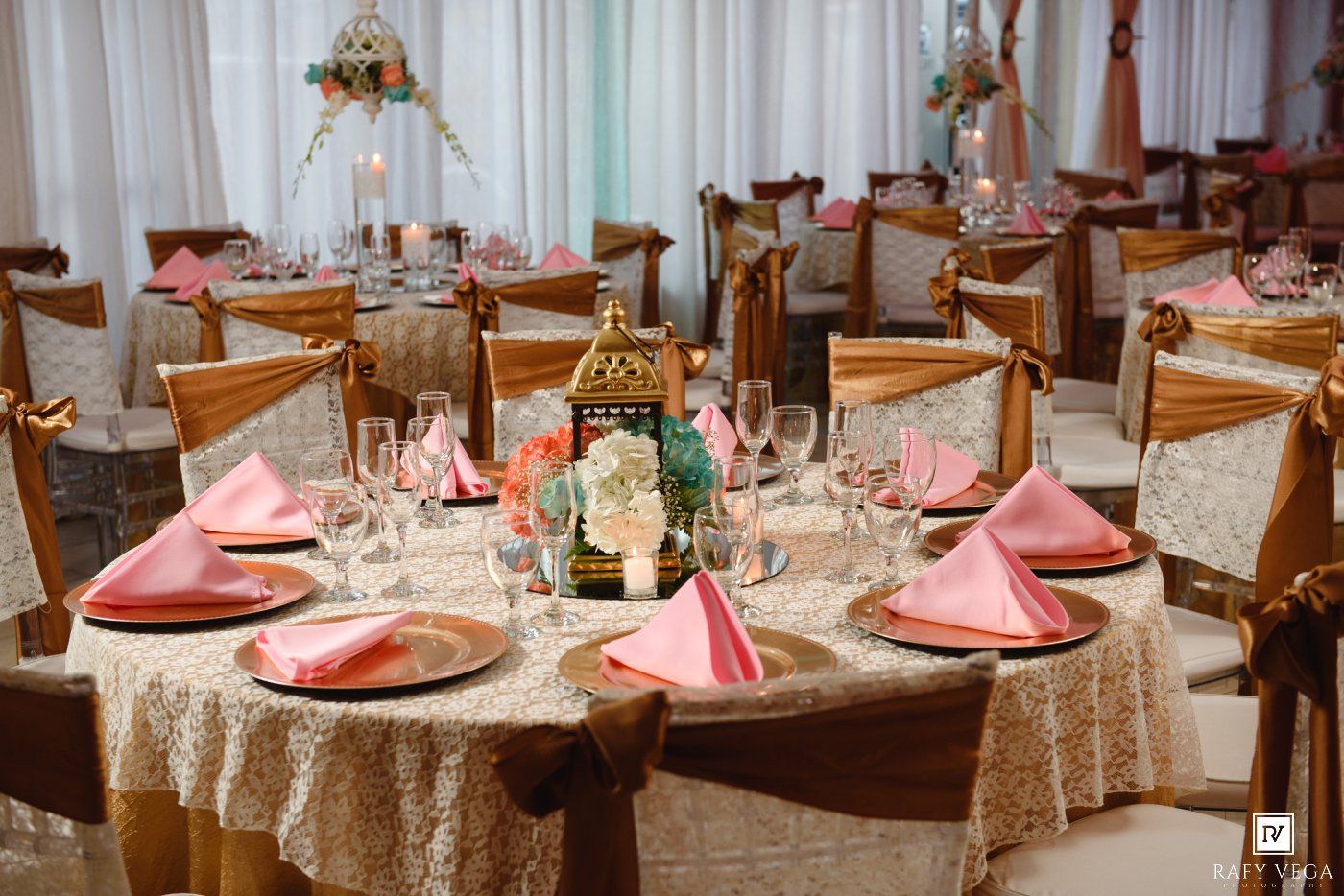 Elegant wedding reception table with pink napkins, gold sequin tablecloth, floral centerpiece, and crystal glassware.