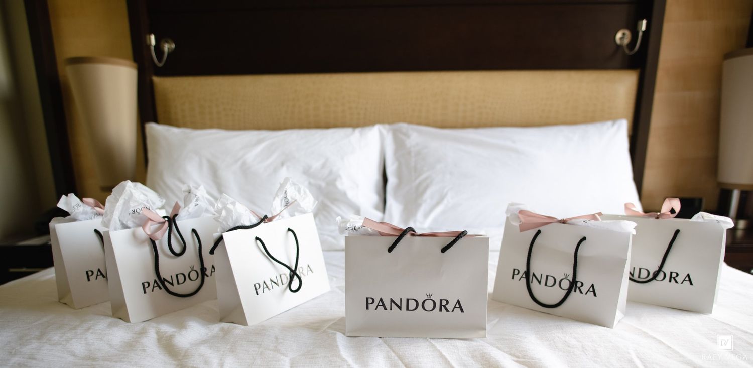 Five Pandora shopping bags with tissue paper arranged on a white hotel bed.